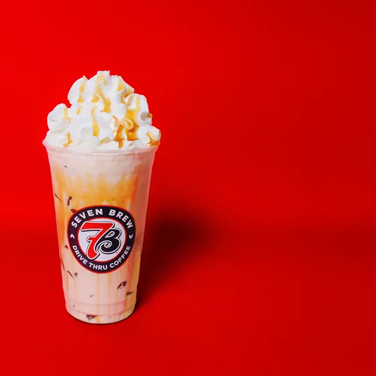 7 Brew short-form post: an iced drink topped with whipped cream and caramel against a solid red background.