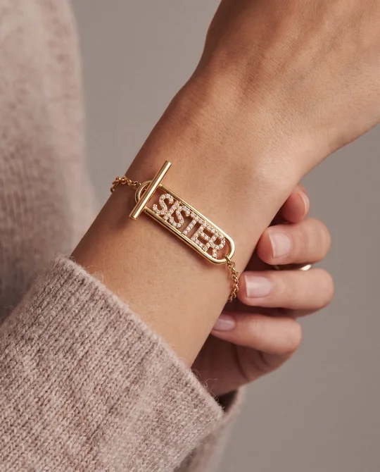 Alex and Ani short-form post: a wrist wearing a gold chain toggle bracelet with a SISTER bar, one hand cupped over the other.