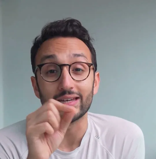 Ali Abdaal short-form post: a man with glasses in a white t-shirt talking to camera at a wooden desk.