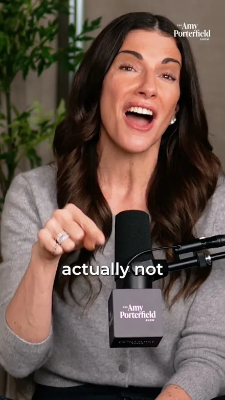 Amy Porterfield short-form post: a woman with long dark hair in a grey cardigan speaking at a podcast microphone.
