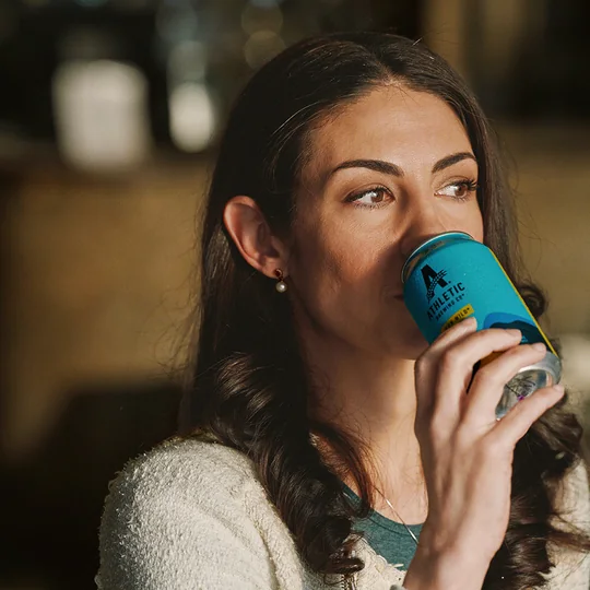 Athletic Brewing short-form post: a woman drinking from a teal Run Wild can in a warmly lit bar.