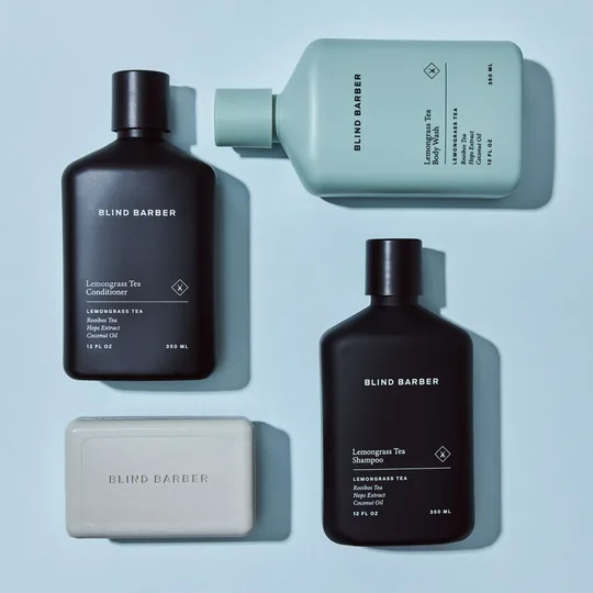 Blind Barber short-form post: black and white grooming bottles, a bar of soap and tubes arranged on a pale blue surface.