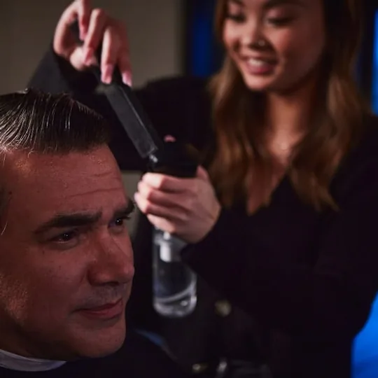 Boardroom Salon for Men short-form post: a smiling stylist working on a man's hair in a blue-lit salon.