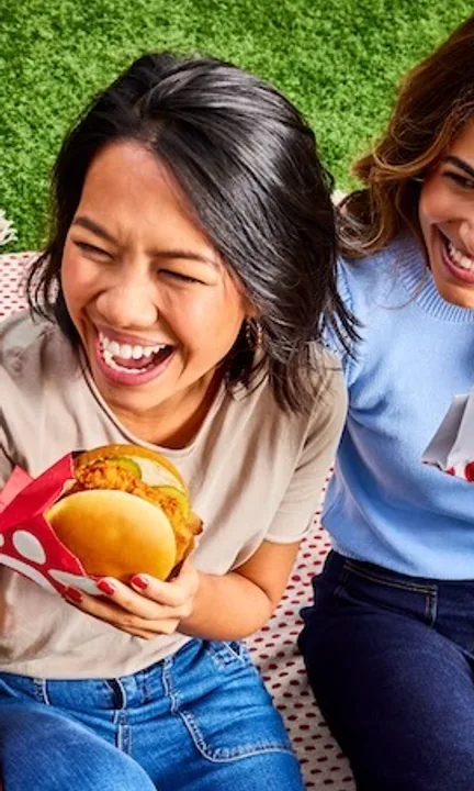 Chick-fil-A short-form post: two friends laughing on a picnic blanket, each holding a chicken sandwich.