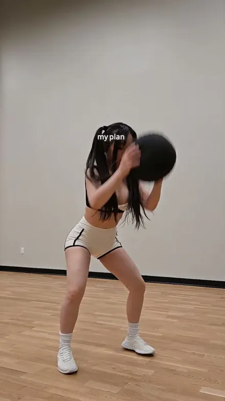 Chloe Ting short-form post: a woman in workout clothes swinging a medicine ball in a bright empty room.