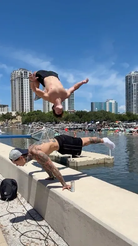 Chris Heria short-form post: a man mid-flip above a dock by the water, with city buildings behind.