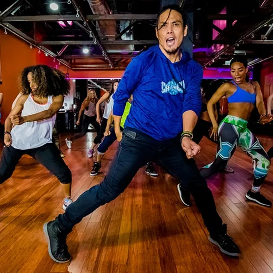 Crunch Fitness short-form post: an instructor in a blue jacket leading a dance fitness class with a bright studio behind.