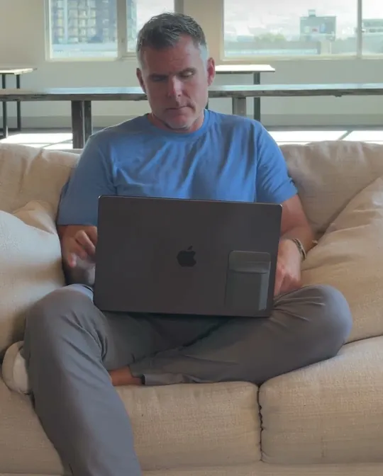 Dan Martell short-form post: a man in a blue t-shirt sitting cross-legged on a couch with a laptop.