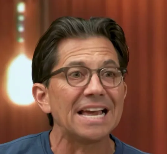 Dean Graziosi short-form post: a man with glasses in a blue t-shirt talking at a podcast microphone.