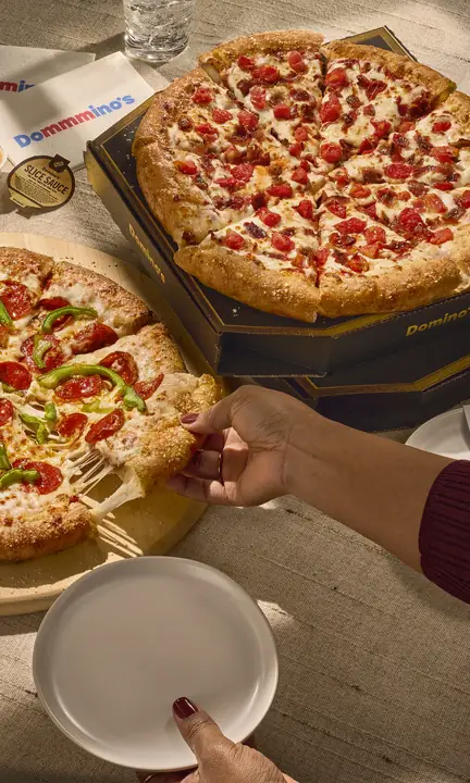 Domino's short-form post: a table of pepperoni pizza, wings and sides with hands reaching in to share.