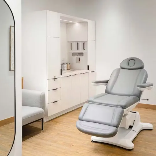Ever/Body short-form post: a bright treatment room with a grey reclining chair, white cabinets and a tall mirror.