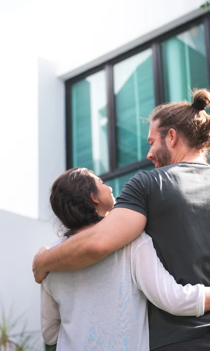 eXp Realty short-form post: a couple with their arms around each other looking out of a large dark-framed window.