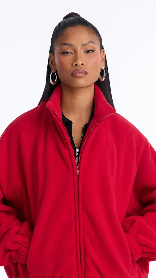 Fashion Nova short-form post: a woman in a bright red fleece zip-up jacket with her hands in the pockets against a white studio background.
