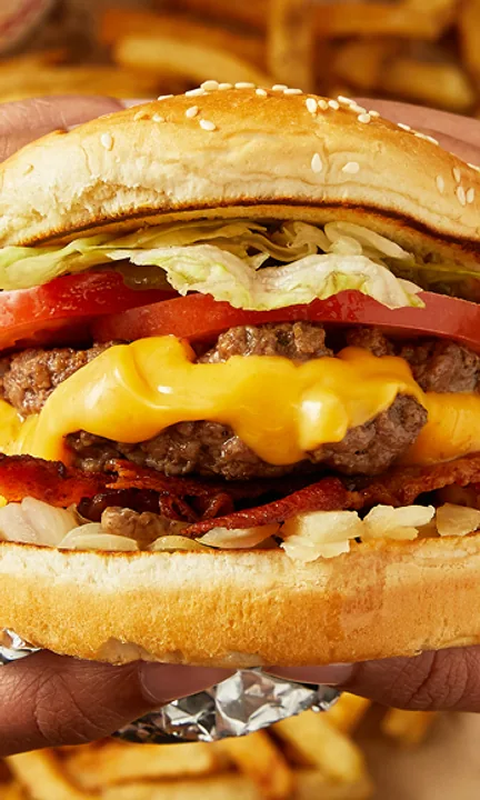 Five Guys short-form post: two hands holding a stacked cheeseburger wrapped in foil above a pile of fries.