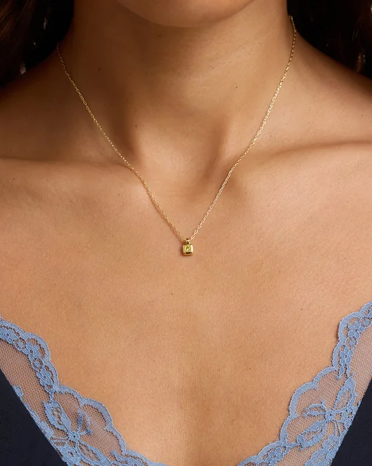 gorjana short-form post: a close-up of a delicate gold necklace with a small birthstone charm resting on a woman's collarbone.