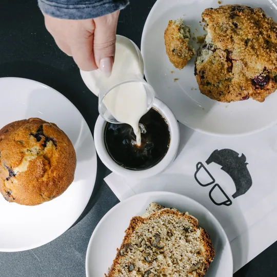 Gregorys Coffee short-form post: a top-down table with a cup of coffee being poured into, a blueberry muffin and a loaf slice.