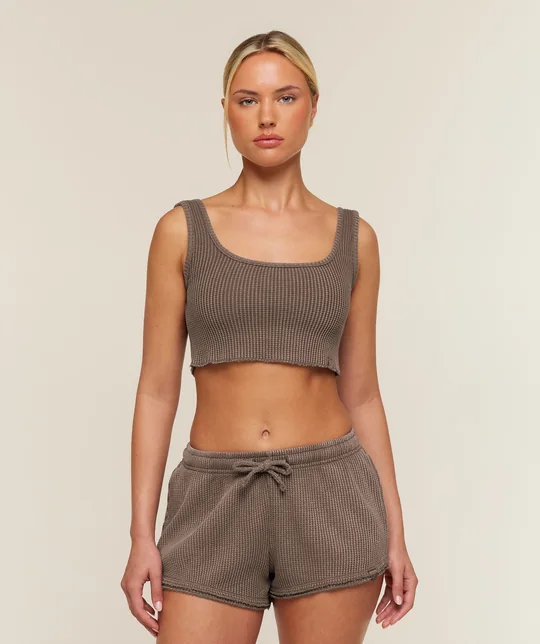 Gymshark short-form post: a model in a soft brown waffle-knit tank and matching shorts against a warm beige studio wall.