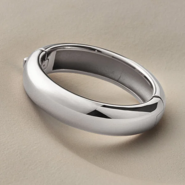 Jenny Bird short-form post: a chunky silver Gemma bangle resting on a warm beige curved surface.