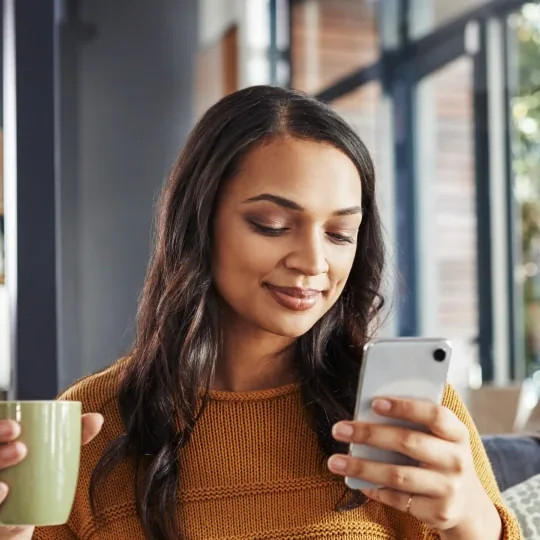 Keller Williams short-form post: a woman in a mustard sweater smiling at her phone while holding a mug.