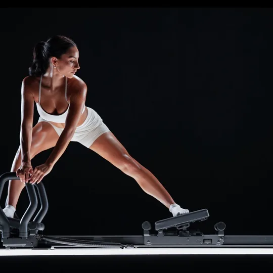 Lagree Fitness short-form post: a woman in white holding a deep side lunge on a black Megaformer against a dark background.