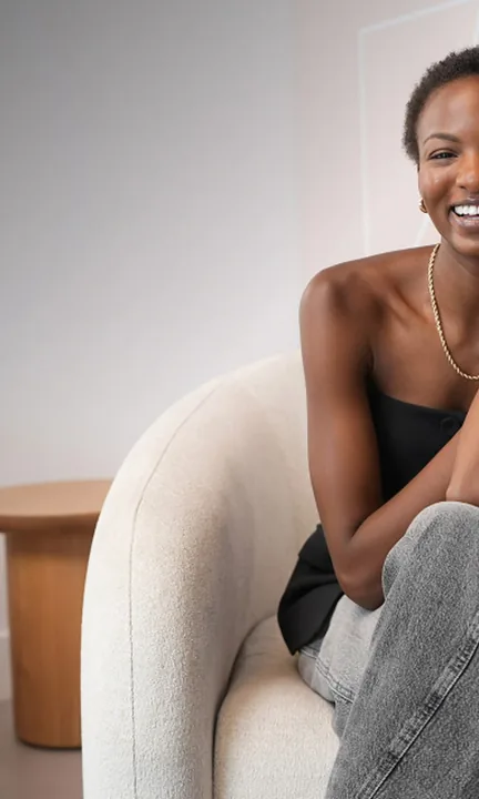 LaserAway short-form post: a smiling woman in a black top and jeans leaning on a cream armchair in a bright room.