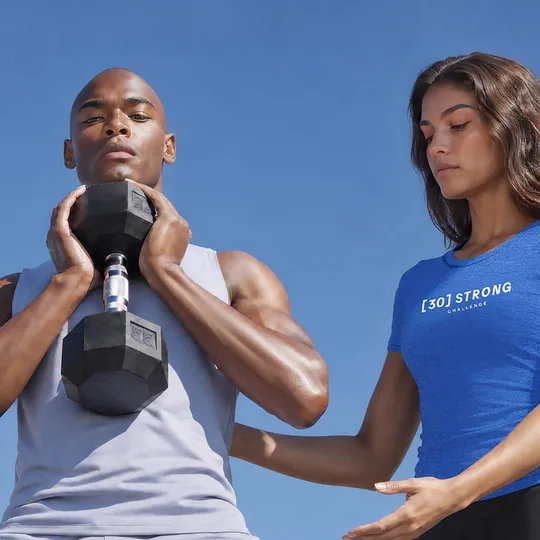 Life Time short-form post: a man holding a dumbbell at his chest next to a woman in a blue Life Time shirt against a blue sky.