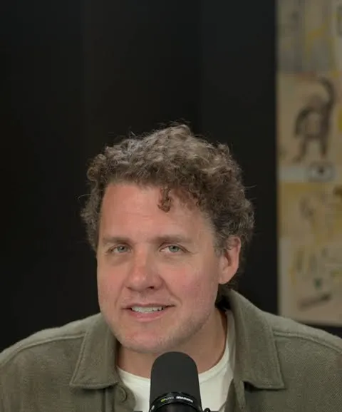 Mark Manson short-form post: a man with curly hair in an olive jacket sitting at a podcast microphone.