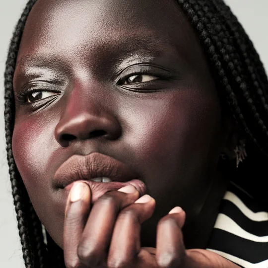 Milk Makeup short-form post: a close-up portrait of a woman with a deep rosy flush on her cheeks, one hand held against her chin.