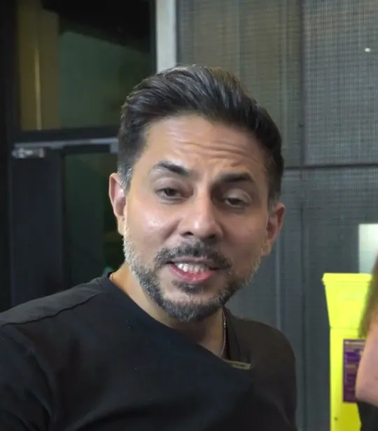 Mindvalley short-form post: a man in a black t-shirt gesturing as he talks in a busy hallway.
