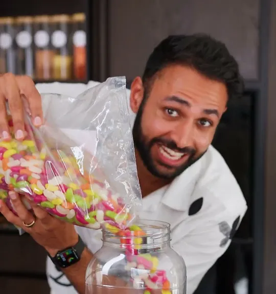 Mrwhosetheboss short-form post: a man in a white jacket tipping a stream of colourful sweets into a glass jar.