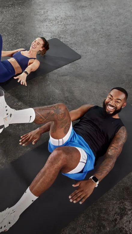 Nike Training Club short-form post: two people laughing during floor exercises on dark mats.