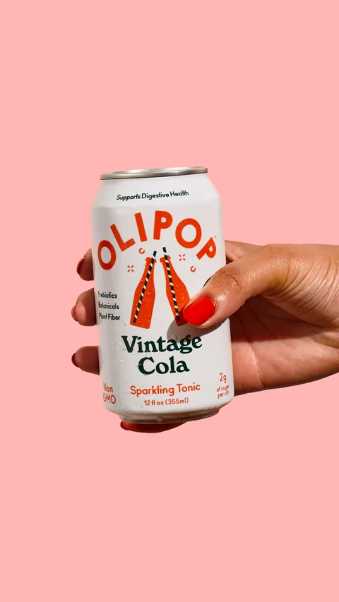 OLIPOP short-form post: a hand with red nails holding a Vintage Cola can against a flat pink background.