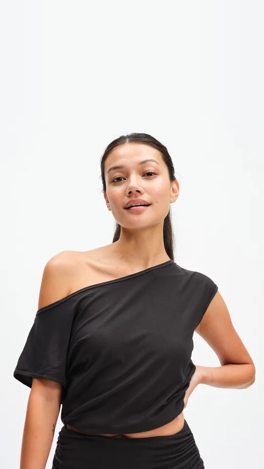 Outdoor Voices short-form post: a smiling woman in a black CloudKnit off-shoulder top with a hand on her hip against a white background.