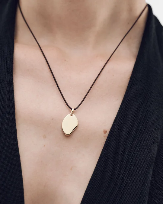 PDPAOLA short-form post: a woman in a black halter top wearing a gold petal-shaped pendant on a dark cord.