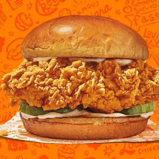 Popeyes short-form post: a crispy chicken sandwich on an orange background with a doodle pattern.
