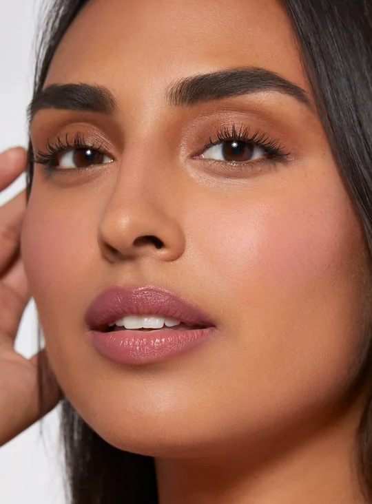 Rare Beauty short-form post: a close-up of a woman with defined brows, her hand raised by her hair and a soft pink flush on her cheek.