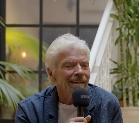 Richard Branson short-form post: a man with white hair in a navy jacket sitting with a microphone among green plants.