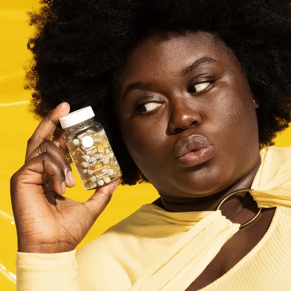 Ritual short-form post: a woman in a cream top holding a Women's Multivitamin bottle up beside her face against a yellow background.