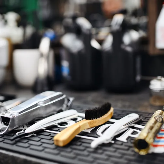 Sharps Barbershop short-form post: clippers, combs, brushes and scissors laid out on a rubber mat at a barber station.