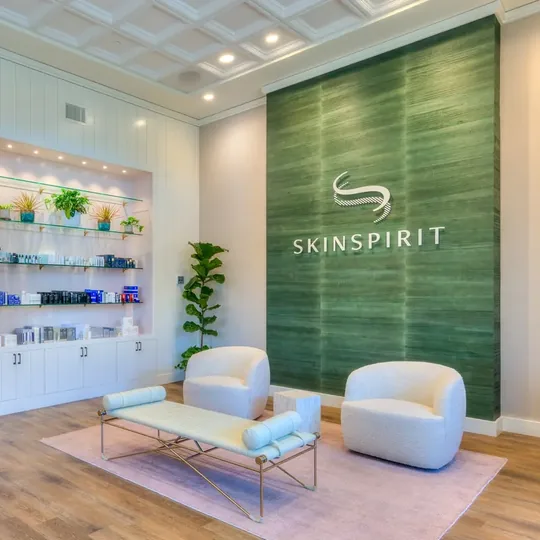 SkinSpirit short-form post: a bright clinic lobby with a green wall, white armchairs and shelves of skin care products.