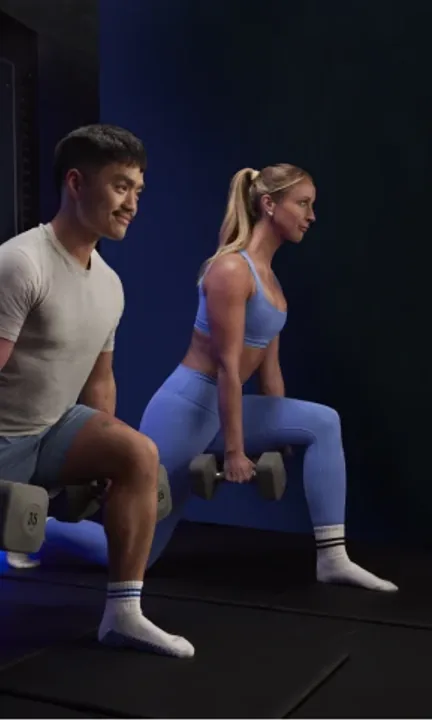 [solidcore] short-form post: a man and a woman holding dumbbells in lunges on a blue-lit reformer.