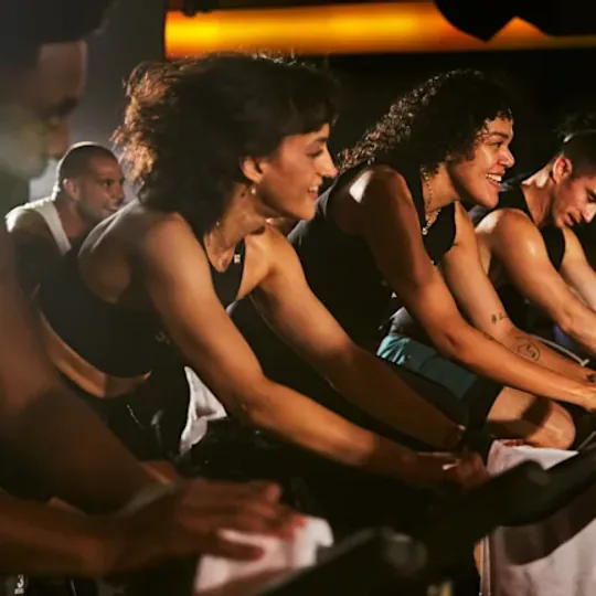 SoulCycle short-form post: a row of riders on indoor cycling bikes in a dimly lit studio.