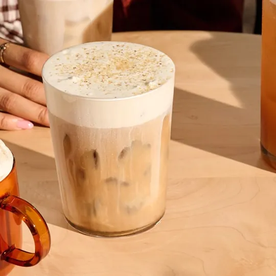 Starbucks short-form post: an iced latte with cold foam on a wooden table beside an amber mug.