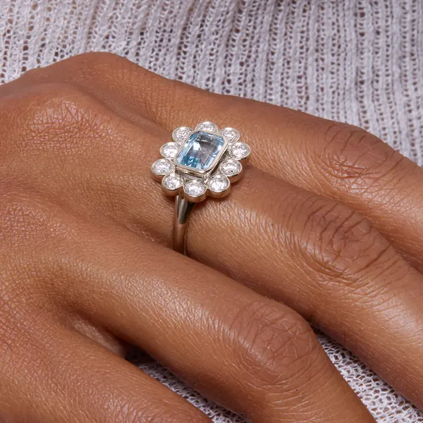 Stone and Strand short-form post: a hand wearing a vintage-style flower ring with a pale blue center stone and diamond-like petals.