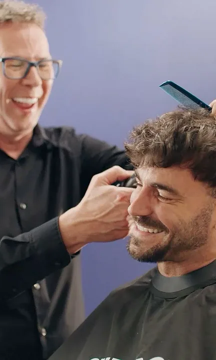 Supercuts short-form post: a laughing stylist in glasses cutting the hair of a smiling man against a purple-blue backdrop.