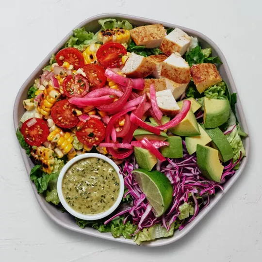 sweetgreen short-form post: a top-down bowl of chopped salad with avocado, tomato and red cabbage next to a small cup of dressing.