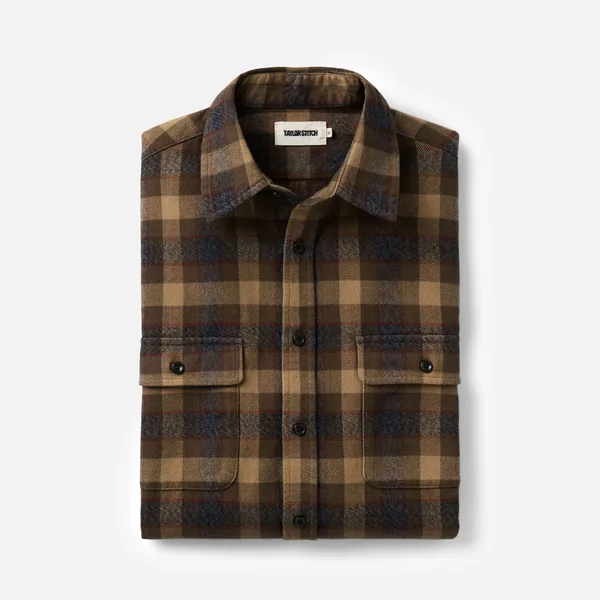 Taylor Stitch short-form post: a folded brown and blue buckeye plaid flannel shirt with two chest pockets on a pale background.