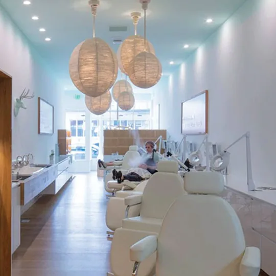 The Face Haus short-form post: a long, bright facial bar with white chairs, wood shelving and woven pendant lights.