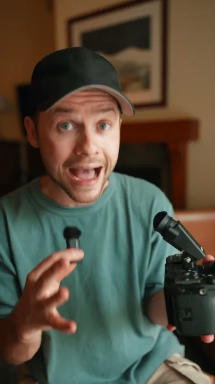 Think Media short-form post: a man in a teal t-shirt and cap holding a camera and a microphone in a cozy room.