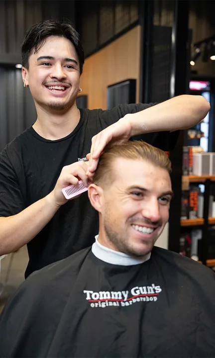 Tommy Gun's short-form post: a smiling barber in black styling the hair of a smiling client in a Tommy Gun's cape.